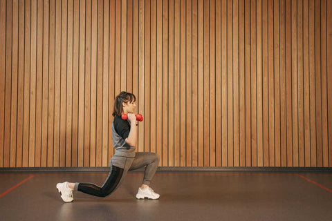 Fandari - la ce ajuta si cum se executa corect_tipuri (cu gantere, in spate) si beneficii pentru picioare_Femeie executand fandari cu gantere intr-o sala de sport