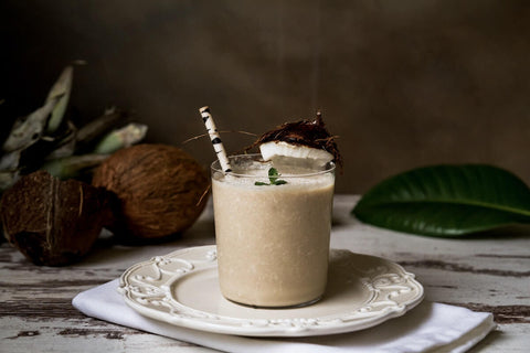 Retete de shake-uri sanatoase - shake in pahar din sticla, nuca de cocos, farfurie alba, o frunza de ficus